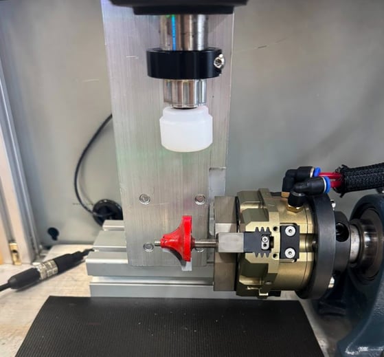 Close-up of a robotic gripper mechanism holding a red router bit next to a vertical ORCA™ Series Smart Linear Motor with a white plastic buffer. 