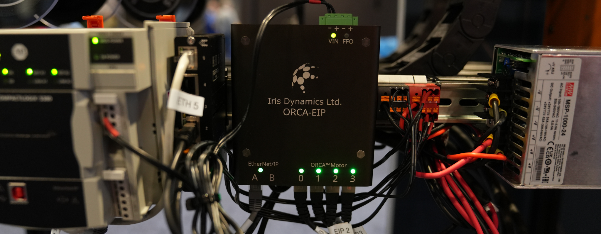 An Iris Dynamics ORCA-EIP EtherNet/IP interface module mounted with connected wiring and active green LED status lights. 